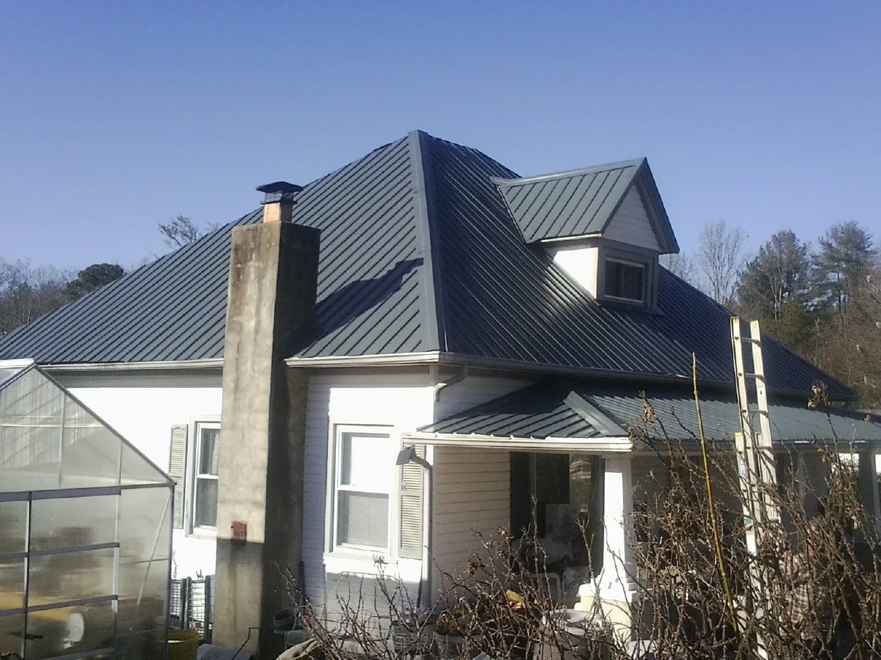 Dark blue standing seam metal roof on a white farmhouse with dormer — Slate & Tile Roof Repair by Roofing Brothers in Crestview