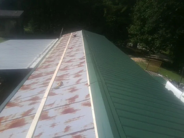 Old rusted panels beside newly installed green metal roofing — Wind Damage Roof Repair by Roofing Brothers in Crestview