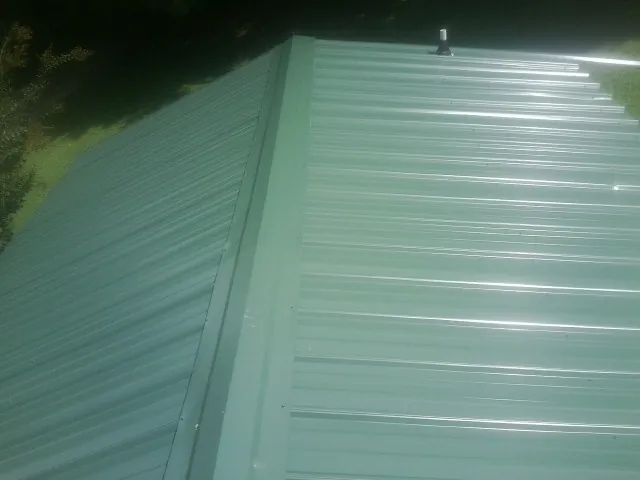 New green metal panels meeting at the ridge of a roof — Flat Roof Repair work by our crew in Crestview