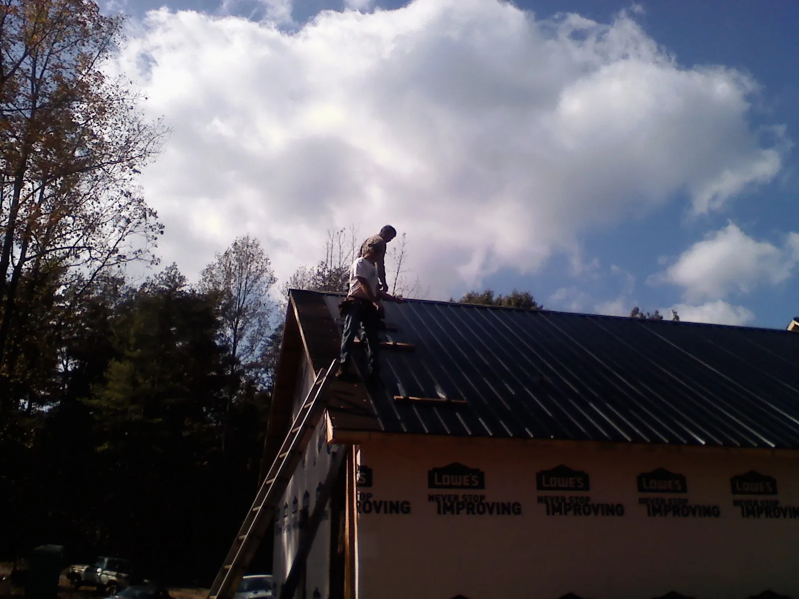 Roofer fastening dark metal panels high against a cloudy sky, from a Roof Inspection job in Crestview